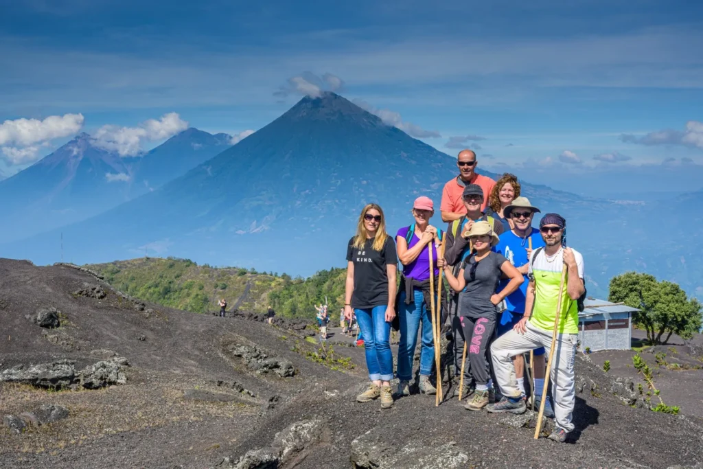 A group of eight people posing with hiking sticks on a rocky slope, with mountains and a blue sky in the background.